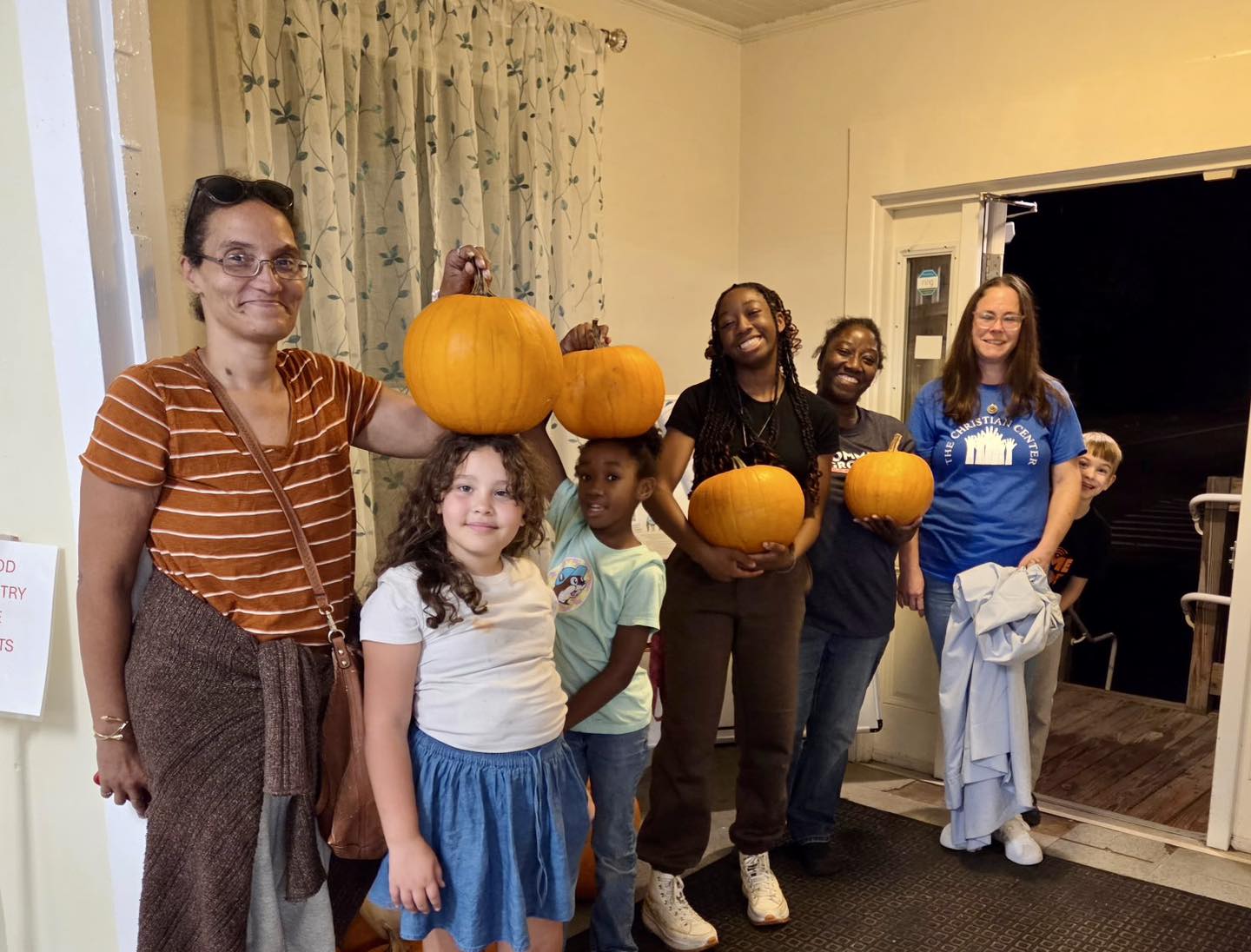 Group holding pumpkins in a room smiling.