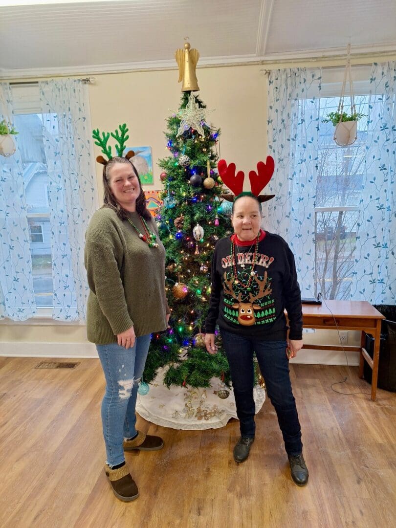 Two people wearing antlers by Christmas tree